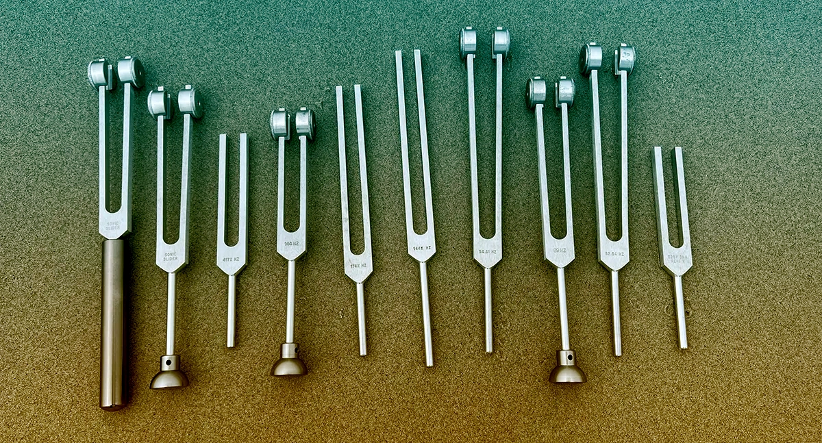 An image of tuning forks on beach sand with a beautiful color gradient overlayed.